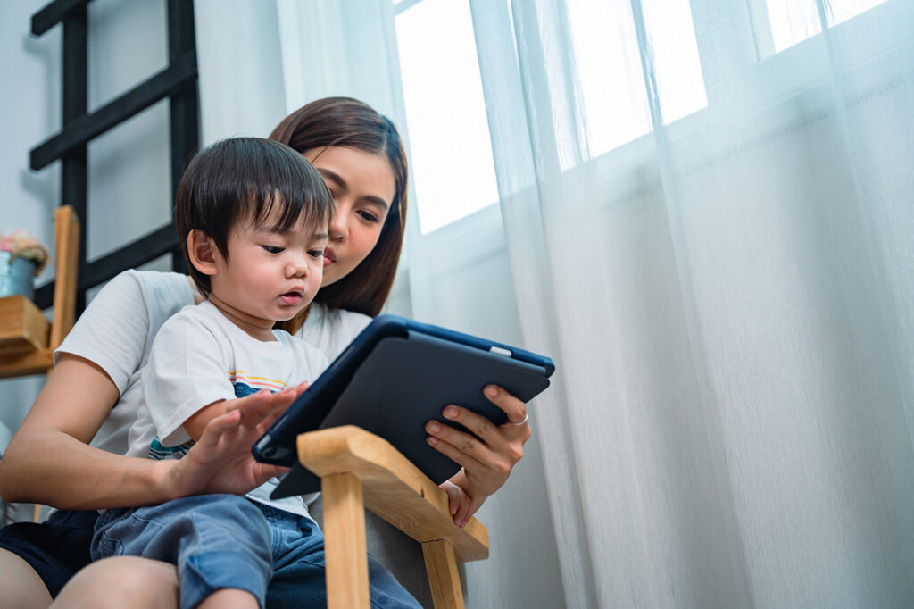 Mother and toddler sitting together reading from a tablet. 